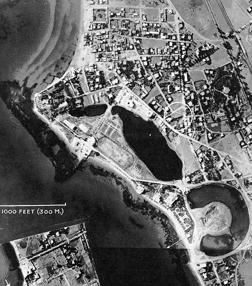 A black and white aerial photograph of an urban area by the siga with a water-filled, torus-shaped inlet.