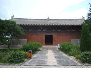 A Chinese temple building that is ret. In front of it is a pathway and trees and flowers.